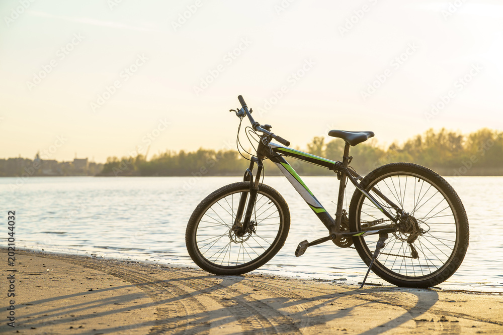 Fototapeta premium A bicycle parked on the riverbank, with sunlight reflecting off the water surface.