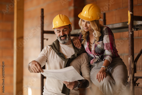 Couple Review Building Plans in a Construction Site During Daytime With Safety Helmets On