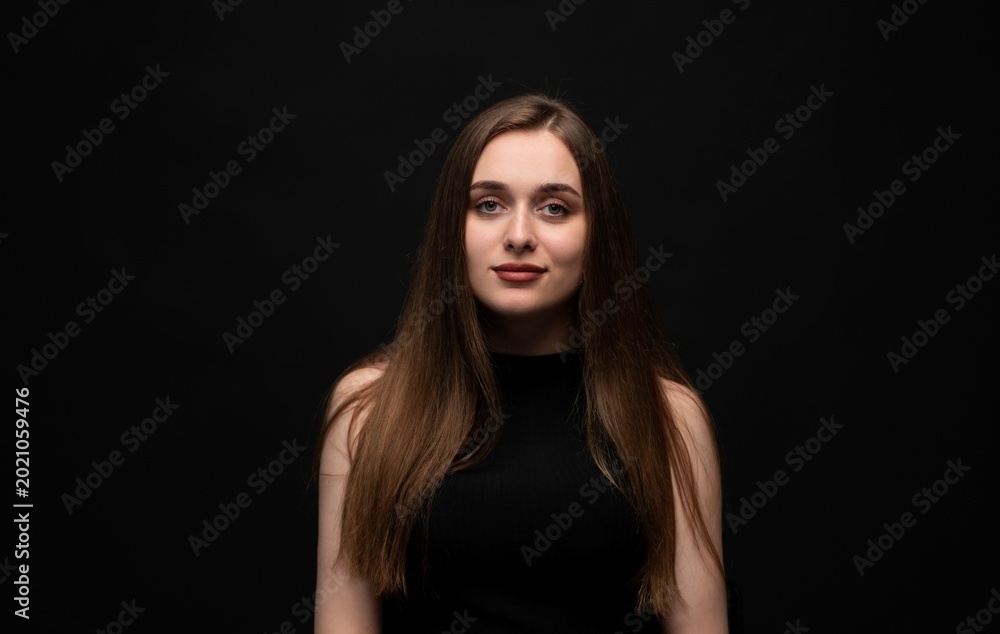 Naklejka premium Young woman portrait with long flowing brown hair looking confident and calm on black background