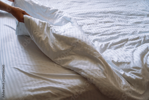 Woman making bed with white duvet in soft light.