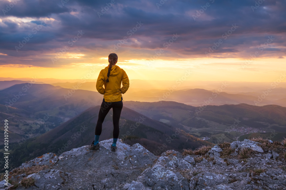 Obraz premium Woman standing on top of a mountain at sunset