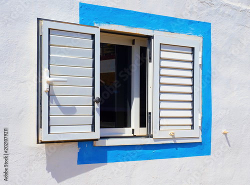 Open white window shutters with blue frame on traditional sunny house facade