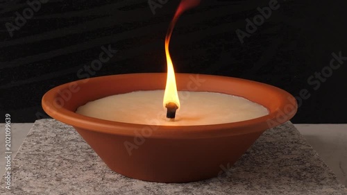 Burning memorial candle in a terracotta bowl on a stone base. Bright flame flickering against a dark background. Symbol of remembrance, mourning, and commemoration during All Saints' Day. 4K video.