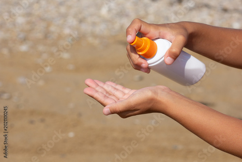 Young hand spraying SPF lotion at the beach shore