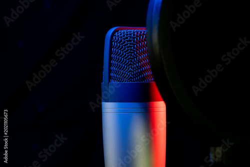 Professional studio microphone with a pop filter against a black background, illuminated by dramatic red and blue lighting