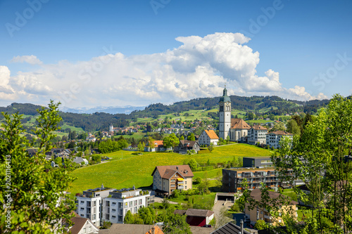 Photos Frühlingshafte Landschaft in Speicher im Appenzellerland mit sanften Hügeln, grünen Wiesen und Kirche unter weitem Himmel