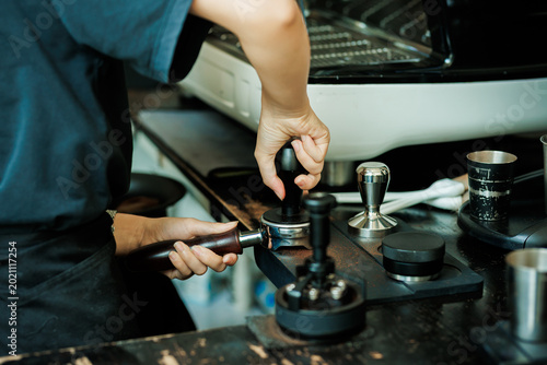 Photos Close-up of a professional barista's hand using a metal tamper to press ground coffee in a portafilter