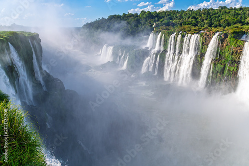 Panoramic scenic view of Iguazu Falls with mist and lush green tropical forest on a sunny day, Misiones Province, Argentina
