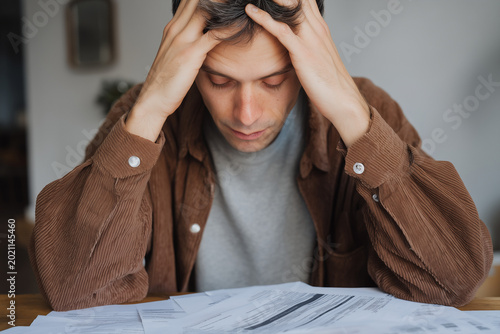 Stressed Young Man Reviewing Legal and Financial Documents at Home Table