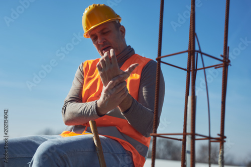 Construction worker having a accident and injured wrist on a construction site outdoors.