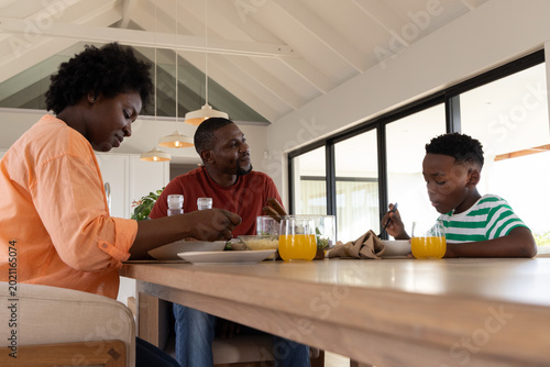 African American family sitting at wooden dining table inside modern home, sharing orange juice