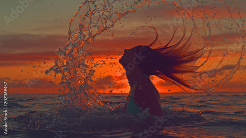 Tableau sur toile SILHOUETTE: Unrecognizable woman flips her long hair back and sprays ocean water