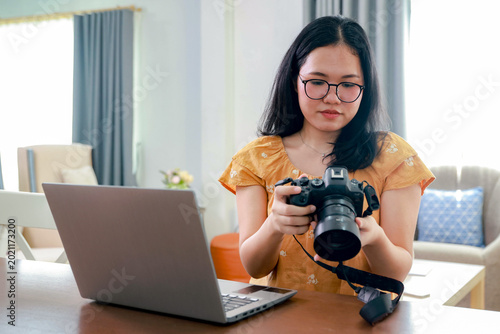Teenage female photographer sits at her home desk reviewing photos stored DSLR digital camera's memory card. She checks for usable images and deletes damaged ones honing photography skills.
