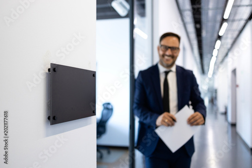 Bild auf Leinwand Businessman in suit walking along modern office corridor, holding papers