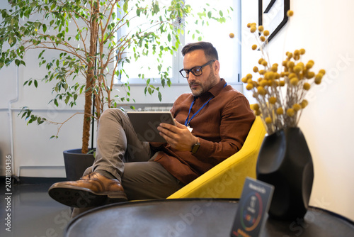 Vászonkép Man using a grey digital tablet, sitting in a contemporary office setting with p