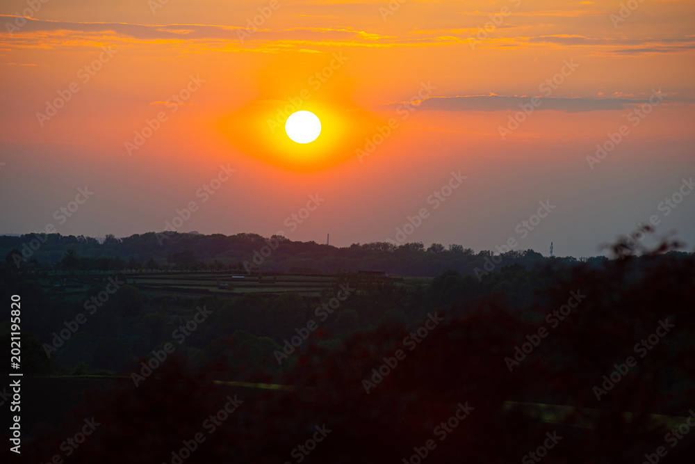 Obraz premium Sundown over fields and trees in a hilly landscape under a colorful evening sky in springtime, Voeren, Limburg, Belgium, May, 2026