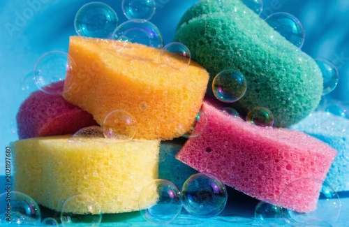 Pile of Bright Sponges and Bubbles. Group of textured foam sponges in various neon colors scattered with soap suds and bubbles in sunlight