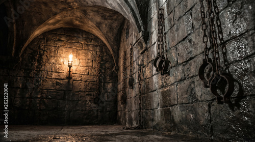 Dark medieval castle dungeon with iron shackles on stone wall and torch light
