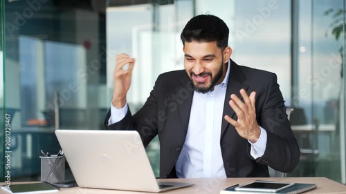 Happy excited businessman received great news on laptop sitting at workplace in business office. Smiling shocked surprised worker celebrating success after reading a positive good message on computer