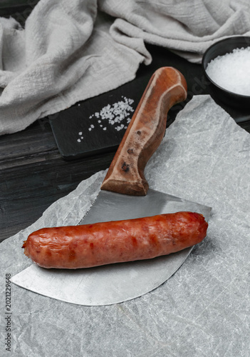 Grilled sausage on a meat cleaver served on parchment paper with coarse salt.