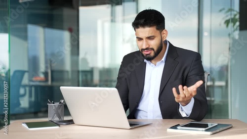 Disappointed businessman having difficulty making transaction using laptop while sitting at desk at workplace in business office. Frustrated confused worker having problems working online on computer