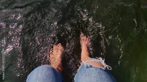 point of view shot woman bare feet splashing and dangling in dark, rippling water lake or river, enjoying relaxing and carefree moment during sunny summer day.