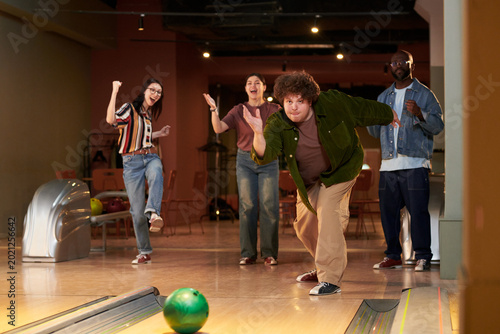 Canvas Print Wide shot of diverse young adults bowling together, cheering strike attempt in leisure venue, showing teamwork and social bonding