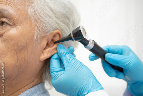 Otolaryngologist or ENT physician doctor examining senior patient ear with otoscope, hearing loss problem.