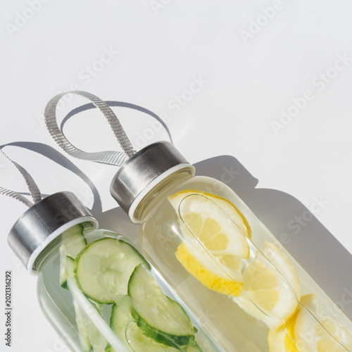 Top view of infused water in glass bottles with lemon and cucumber, modern minimal layout. Takeaway home made healthy detox drink with natural ingredients for sport, fitness, everyday self care.