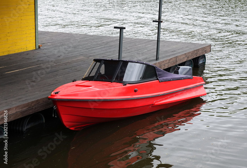 Red motorboat with outboard petrol engine docked at wooden pier on calm water side view
