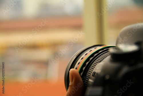 Tableau sur toile Closeup of a professional DSLR camera lens with colorful rings held by a photographer, featuring a soft blured urban background