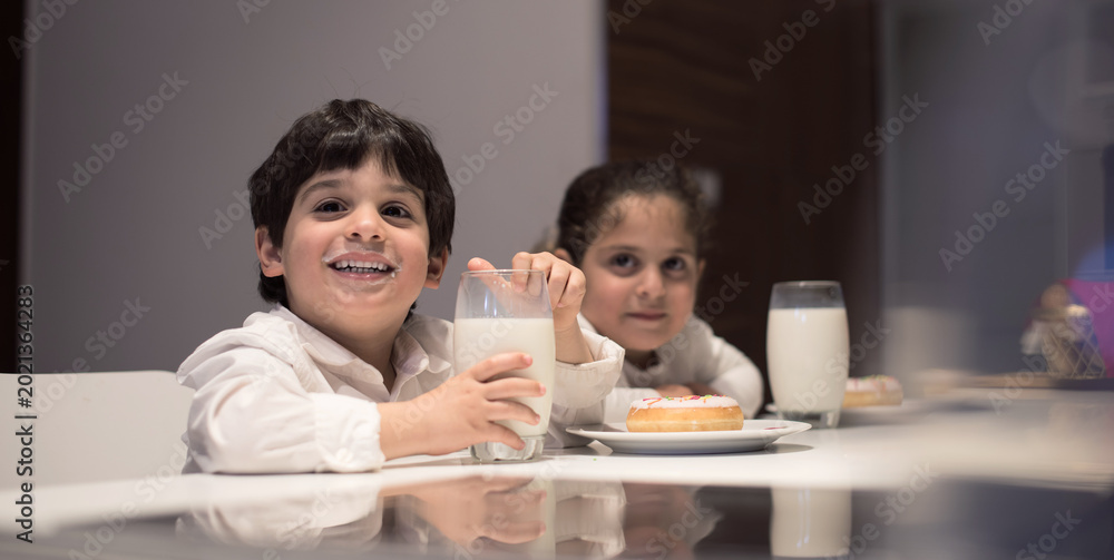 Fototapeta premium Middle Eastern family sharing iftar dinner at home with children drinking milk and enjoying donuts