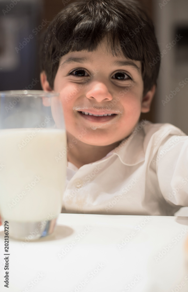 Fototapeta premium Smiling child with milk moustache holding a glass at modern home iftar during Ramadan Eid dinner