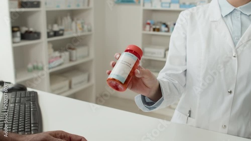 Close up shot of unrecognizable young woman as pharmacist handing bottle of pills to customer while selling medication over checkout counter at pharmacy, copy space