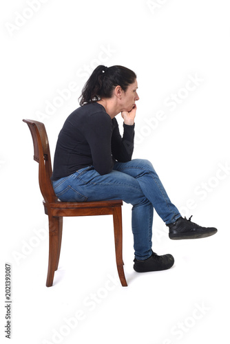 side  view of a woman sitting in a chair hand on chin and cross legged on a white background