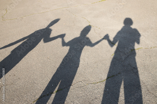 Shadow silhouettes of three people holding hands on the pavement on a sunny day. Friendly family relationships, positive atmosphere, family togetherness on a walk. unity and mutual support
