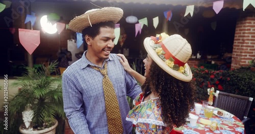 Joyful Brazilian couple dancing together at a traditional Festa Junina celebration wearing straw hats and colorful costumes under festive flags during a lively outdoor party event in Brazil