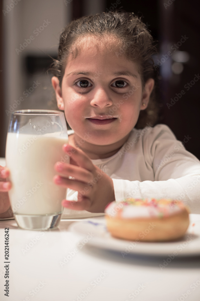 Fototapeta premium Young girl enjoying milk and a donut at a modern family iftar dinner during Ramadan Eid celebration