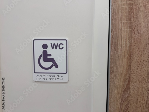 Photos Accessible restroom sign featuring a wheelchair symbol and braille, affixed to a