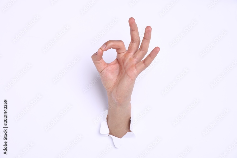 Naklejka premium Man showing ok gesture through hole in white paper, closeup