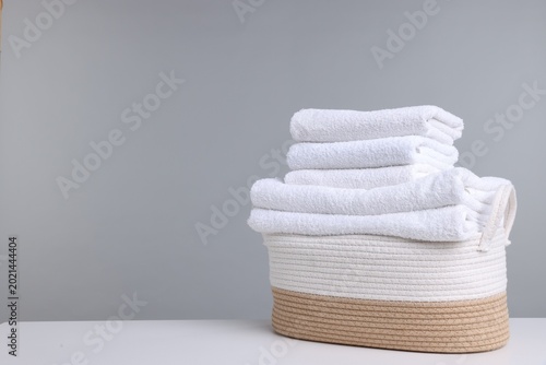 Soft clean towels in laundry basket on white table against light grey background. Space for text