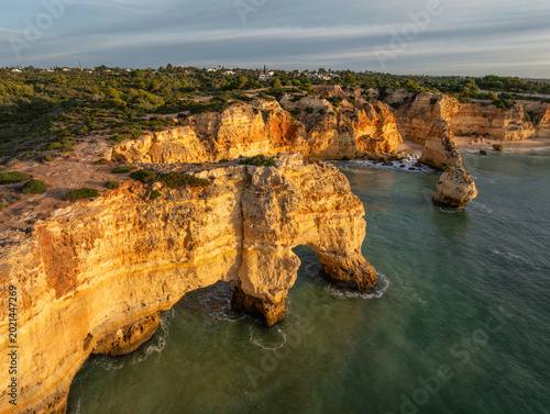 Drone view of Praia da Marinha beach in Algarve, Portugal, with golden cliffs, sea arches, turquoise Atlantic water, and coastal rock formations.