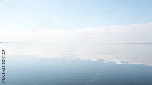 Calm water surface reflecting a clear sky with soft clouds and distant horizon