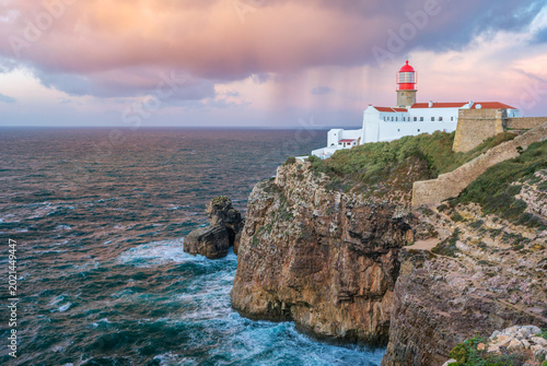 View of the Lighthouse of Cabo de Sao Vicente in Sagres, Algarve, Portugal, at sunrise with Atlantic ocean, cliffs, and cloudy sunrise ocean