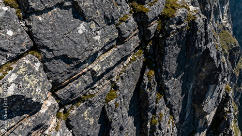 Rugged rocky cliff face with moss and lichen under bright sunlight