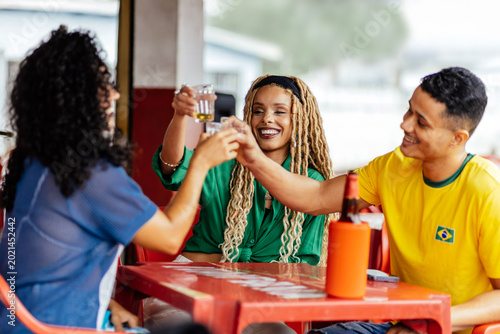 Brazilian friends enjoying drinks and watching football together at a casual bar, celebrating and socializing in a vibrant atmosphere.