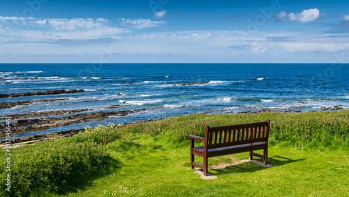 Foto Un banc vide face à la mer du Nord sous le ciel bleu à côté de Brough of Birsay,