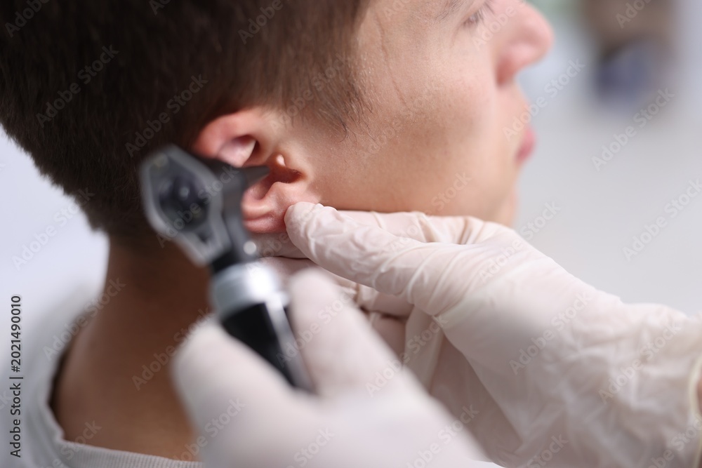 Fototapeta premium Hearing test. Doctor examining man's ear with otoscope in clinic, closeup