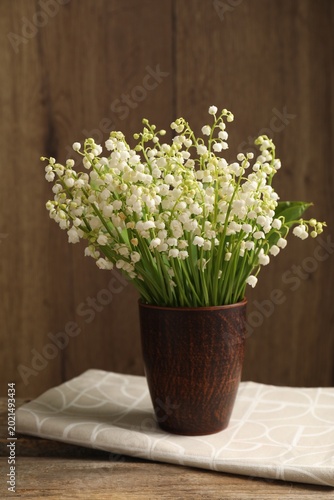 Beautiful lily-of-the-valley flowers in vase on wooden table, closeup