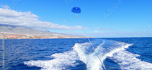 фотографія Colorful parasail soaring behind motorboat across Atlantic Ocean near Tenerife coast with mountain panorama and bright blue sky